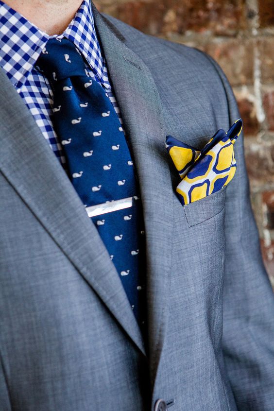 a bold and cool groom's outfit with a blue and white checked shirt, a navy and white whale print tie, a grey blazer and a printed handkerchief