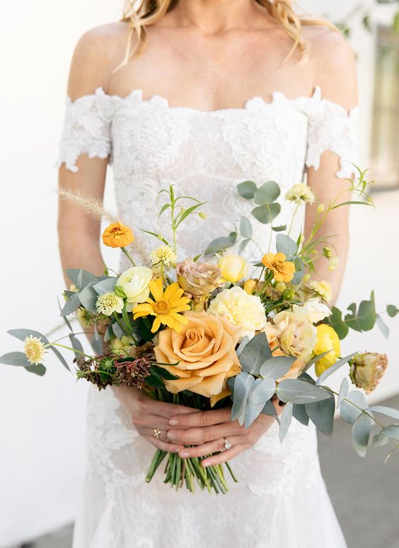 a bold wedding bouquet of yellow and peachy blooms, greenery and grasses looks textural, catchy and dimensional