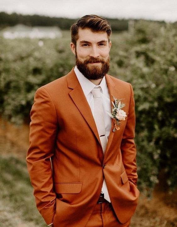 a bright rust-colored suit, a white shirt, a creamy tie and a florla boutonniere for a chic and stylish fall groom's look