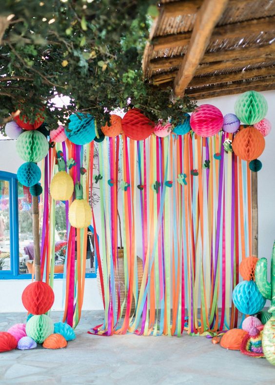 a bright wedding backdrop of colorful ribbons and colorful honeycomb pompoms is a fun idea for a festival wedding