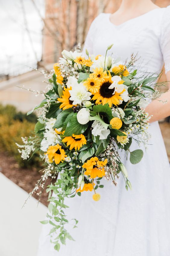 a bright wedding bouquet with sunflowers, white dahlias, greenery, blooming twigs and branches and cascading greenery