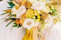 a bright yellow wedding bouquet of billy balls, ranunculus and peony roses, yellow leaves and ribbons is gorgeous
