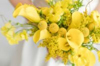 a bright yellow wedding bouquet of callas, mimosas and billy balls plus some twigs strikes with its color