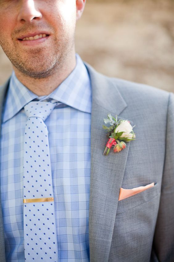 a chic groom's outfit with a blue checked shirt, a white and blue polka dot tie, a grey blazer and a neutral boutonniere