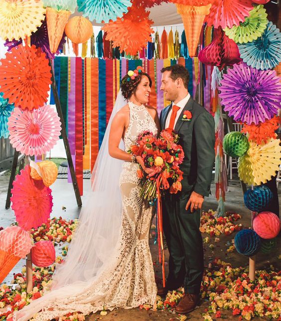 a colorful paper pompom and fan wedding arch and lots of blooms on the floor for a festival-themed wedding