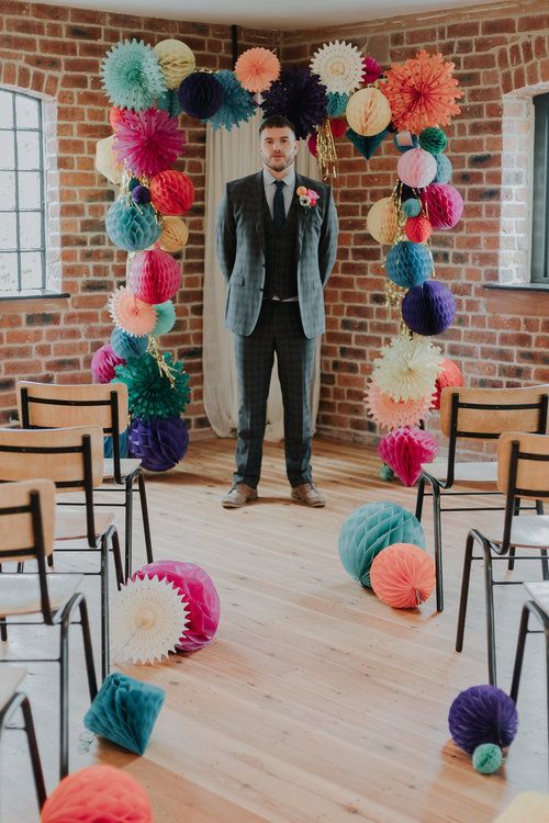 a colorful paper pompom and fan wedding arch with gold fringe is a very bold and cool idea to rock