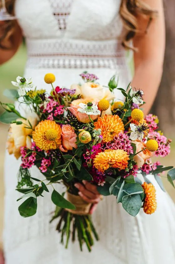 a colorful summer wedding bouquet of yellow roses and dahlias, bold pink fillers, billy balls and greenery