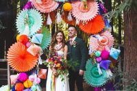 a colorful wedding arch covered with bright paper fans and honeycomb pompoms and rhombs is a fun idea