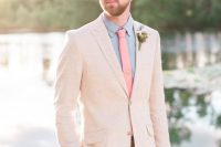 a creamy pantsuit, a blue shirt, a coral skinny tie and a neutral and pastel floral boutonniere compose a lovely look for a summer wedding