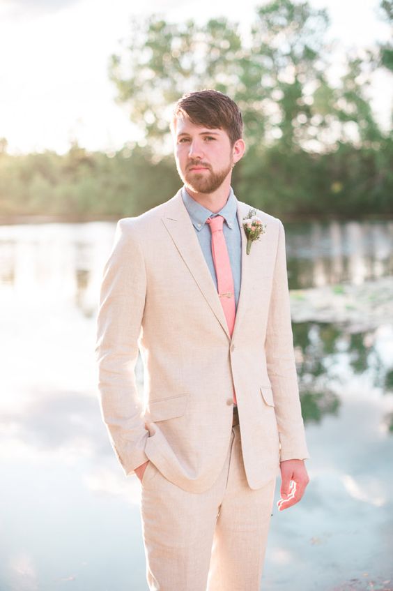 a creamy pantsuit, a blue shirt, a coral skinny tie and a neutral and pastel floral boutonniere compose a lovely look for a summer wedding