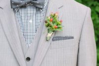a dove grey three-piece suit, a gingham shirt, a grey polka dot bow tie and a berry and greenery boutonniere