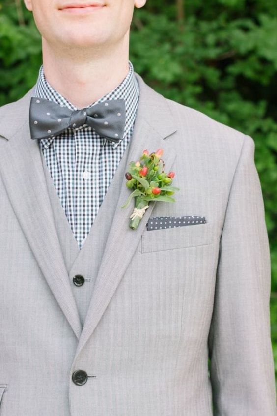 a dove grey three-piece suit, a gingham shirt, a grey polka dot bow tie and a berry and greenery boutonniere