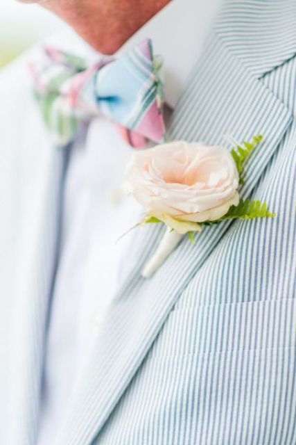 a dreamy and airy groom's look with a blue thin striped blazer, a white shirt, a bold checked bow tie and a blush boutonniere