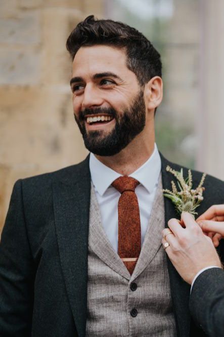 a fall boho groom's outfit with a white shirt, a grey waistcoat, a graphite grey blazer and a rust skinny tie plus a greenery boutonniere