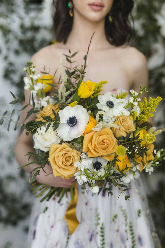 a fall wedding bouquet of yellow roses and tulips, ranunculus, white anemones and roses, greenery and billy balls for spring
