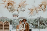a fun boho wedding dance floor with letters on it, with pampas grass, white orchids and disco balls over the dance floor is wow