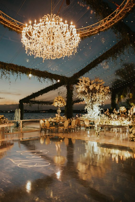 a glam dance floor with a glossy cover and monograms, an oversized chandelier and string lights over the space