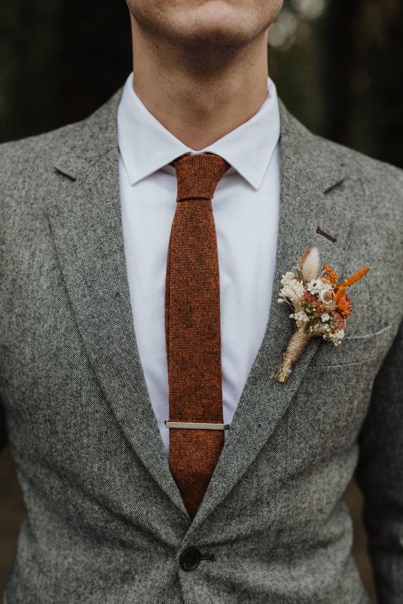 a grey pantsuit, a white shirt, a rust colored tie and a matching rust and neutral floral boutonniere are a cool outfit for a fall wedding
