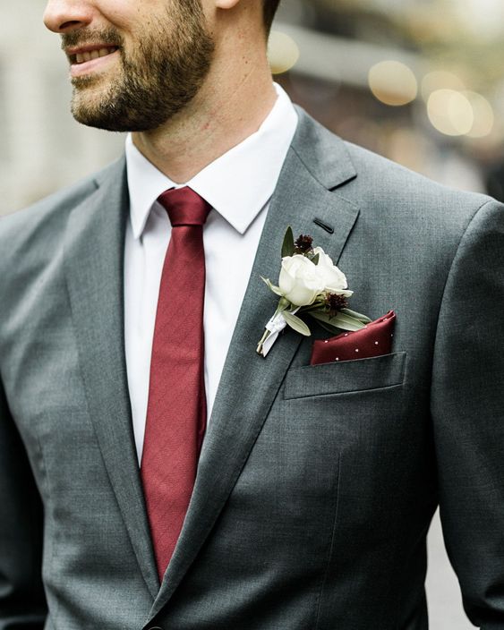a grey pantsuit, a white shirt and a burgundy tie plus a burgundy handkerchief and a white floral boutonniere
