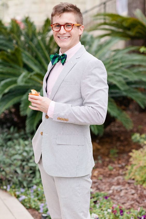 a grey thin striped suit, a pink shirt and a navy and green striped bow tie for a bold and fun outfit at the wedding
