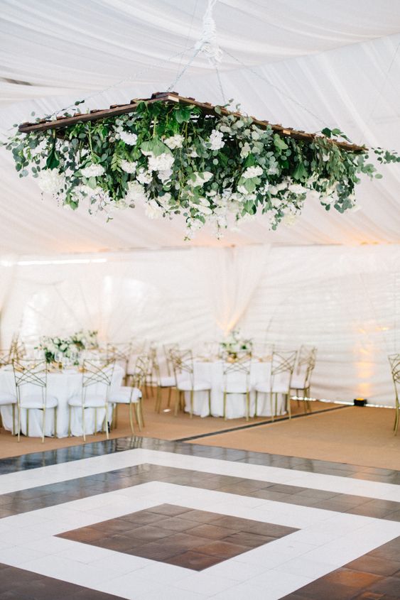 a modern black and white dance floor, with a large greenery and white bloom chandelier over the space