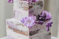 a naked wedding cake decorated with purple blooms and topped with a purple macaron