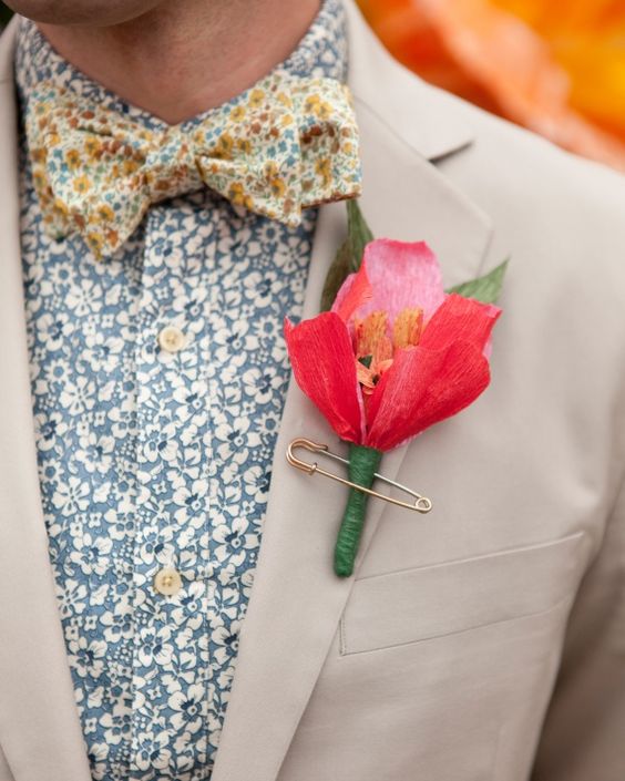 a navy suit, a blue floral print shirt, a grey and yellow floral print bow tie and a bold paper bloom for a unique personalized look