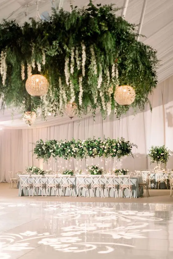 a playful glam dance floor with lights, an oversized chandelier with greenery and white blooms, glam sphere pendant lamps