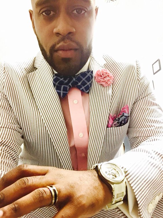 a pretty groom's outfit with a striped blazer, a pink shirt, a navy checked bow tie and a bright blue and pink handkerchief