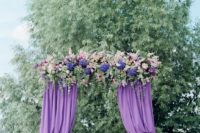 a purple wedding arch with curtains, lush blooms and greenery looks very eye-catching