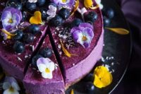 a purple wedding cheesecake with edible flowers and blueberries