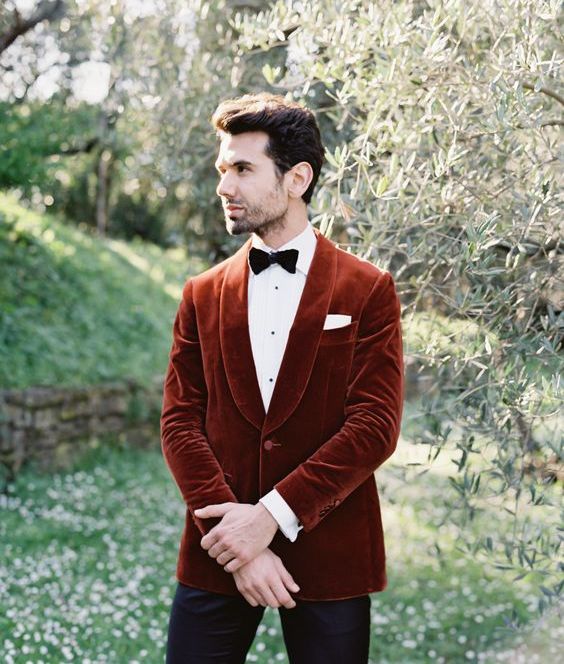a rust vevlet blazer, a white shirt, a black bow tie and black pants for a bold and chic fall groom's look