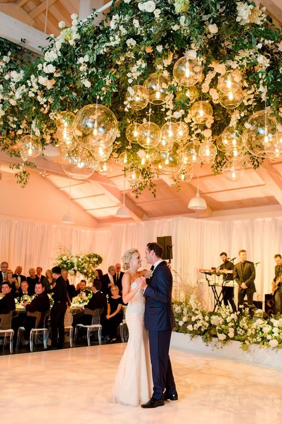 a sophisticated wedding dance floor with white blooms around and over it, with greenery and clear glass sphere pendant lamps is amazing