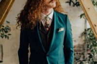 a turquoise suit, a black waistcoat and a white shirt with a floral tie plus long copper curls for a statement boho groom’s look