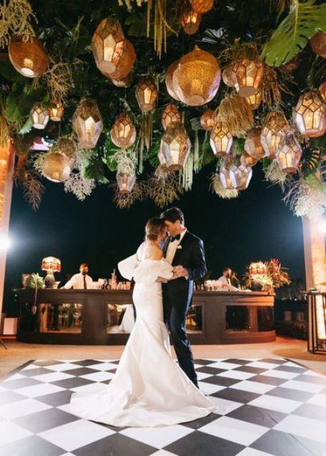 a wedding dance floor in black and white, with tropical greenery, faceted pendant lamps over it is amazing