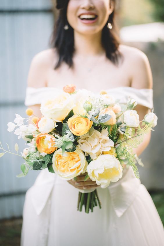 a yellow wedding bouquet of peony roses and ranunculus, greenery and some fern is ideal for spring or summer