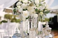 an elegant and shiny silver wedding centerpiece of mercury glass jars, vases and white lush blooms