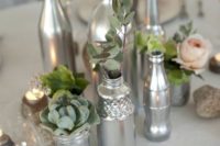 silver jars and bottles as vases for some herbs and blooms are great to compose a chic winter wedding centerpiece