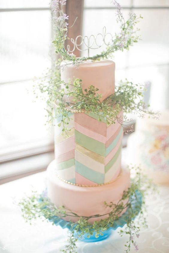 a blush wedding cake with a pastel chevron tier that adds interest to it, with greenery and a wire cake topper is a gorgeous idea for a spring wedding