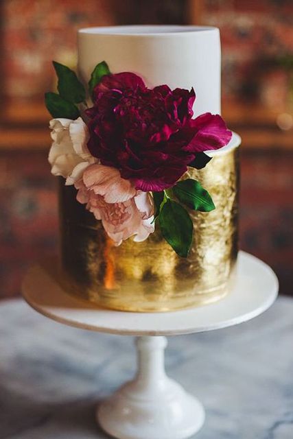 a bold wedding cake with a white and gold leaf tier and white, blush and purple blooms is very refined