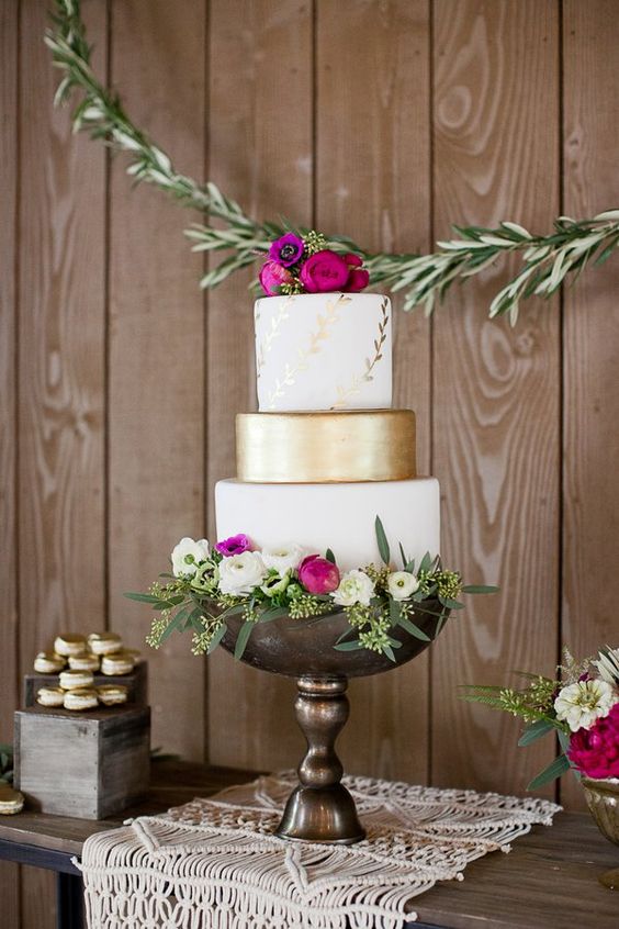 a bright and refined wedding cake with white and gold tiers, botanical patterns, bright blooms, white flowers and greenery