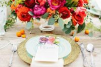 a bright floral wedding centerpiece in red, orange, fuchsia and some greenery plus privet berries