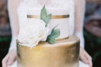 a classic elegant wedding cake with a white and gold tier, with a large white sugar bloom and leaves