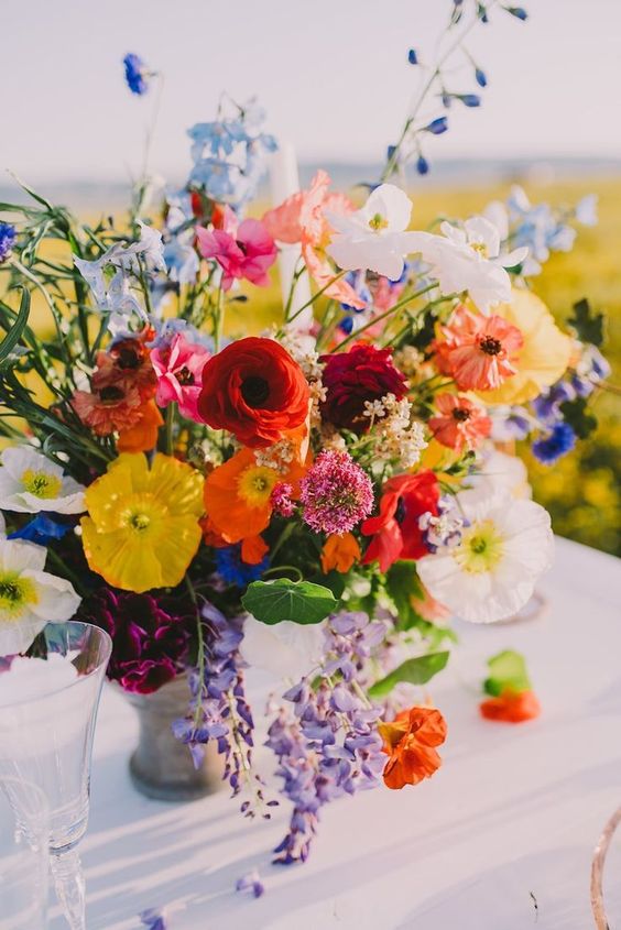 a colorful floral wedding centerpiece in yellow, red, orange, purple and blue and some greenery for spring