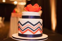 a colorful wedding cake with navy ribbon, navy and orange chevron painted decor and a coral sugar bloom on top is great for a colorful wedding