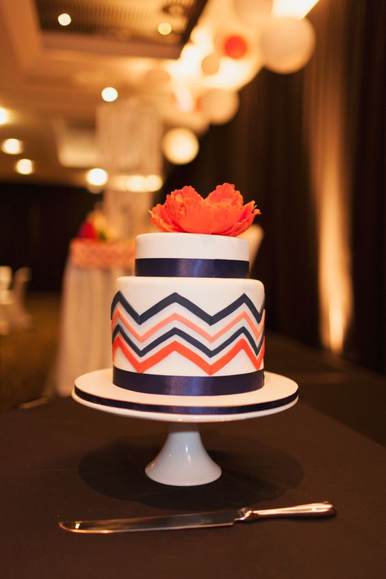 a colorful wedding cake with navy ribbon, navy and orange chevron painted decor and a coral sugar bloom on top is great for a colorful wedding