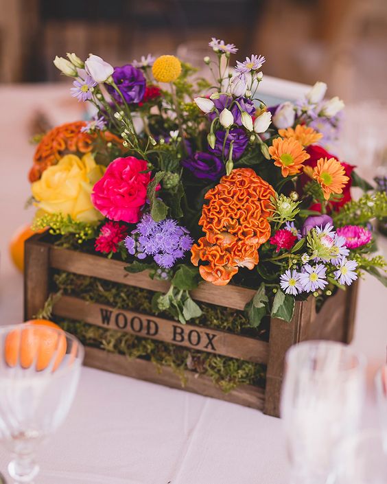 a colorful wedding centerpiece of a wooden box with moss, yellow, marigold, purple and hot pink blooms