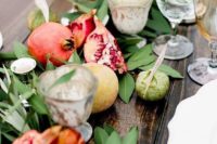 a fall wedding table runner of greenery, apples, pomegranates and candles is a very lush and cool idea