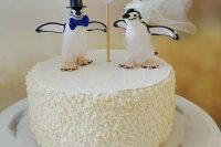 a fun white buttercream wedding cake with cheerful penguin toppers showing off the couple and a heart topper is amazing