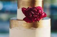 a glam white and gold brushstroke wedding cake with a burgundy bloom and a gold arrow cake topper with monograms and a heart is a cool idea